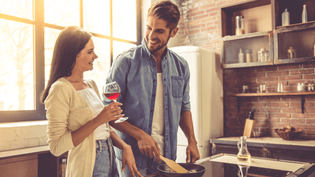 キッチンで料理をする男性とワインを飲む女性
